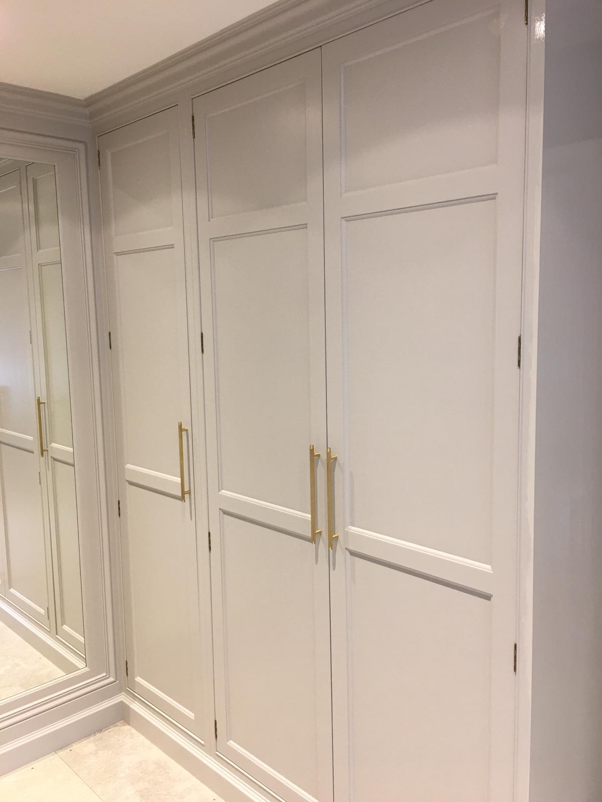 Light painted fitted wardrobes with panelled doors, brass handles and a full-height mirror