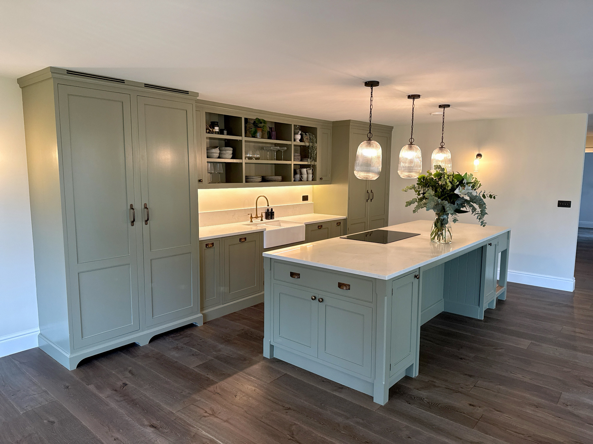 Soft green painted kitchen with a central island, open dresser shelving and pendant lighting
